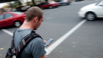 RSE tecnológica: un peatón imprudente cruza una calle si sacar la vista de su celular.